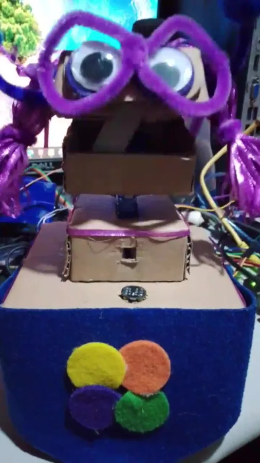 Kai, a cardboard robot with googly eyes and purple yarn pigtails, mirroring a face on the DEVCON 17 stage