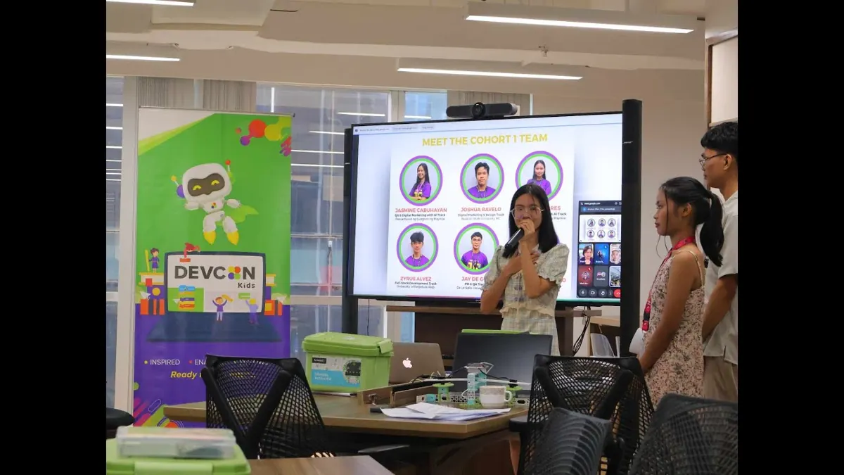 Interns presenting the Cohort 1 team to an audience, with a DEVCON Kids banner